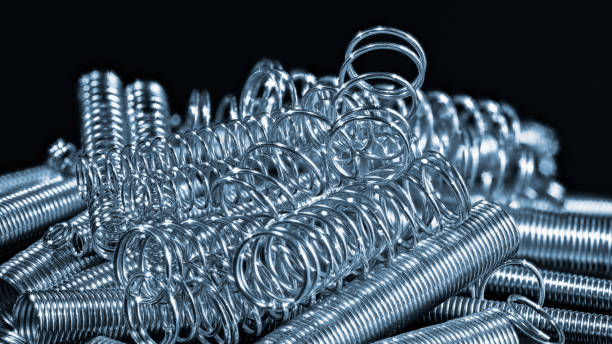 Elastic stainless steel compression and extension coil springs. Helical wire winding detail Abstract pile of shiny flexible tension metal parts on black background. Detail of springy machine components. Mechanical engineering coiled spring stock pictures, royalty-free photos & images