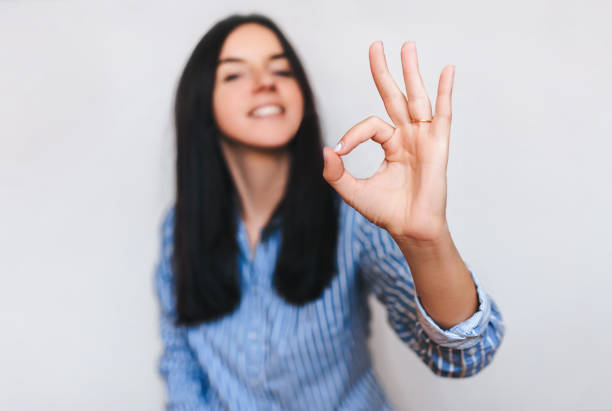 Beautiful young happy smiling girl in blue shirt showing ok sing with her hand. OK concept. Beautiful young happy smiling girl in blue shirt showing ok sing with her hand. OK concept. Isolate. Copy space. no brainer sign stock pictures, royalty-free photos & images