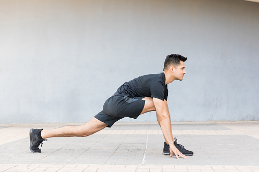 Handsome male athlete doing low lunge stretch on sidewalk
