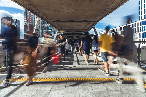Motion blur of crowded Asian people walking on elevated public walkway. Commuter lifestyle, Asia city life, or pedestrian transportation concept