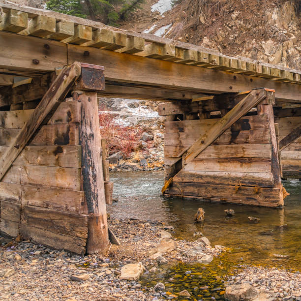 istock Square frame Rustic wooden bridge overlooking lush trees on a mountain under cloudy sky 1153515835