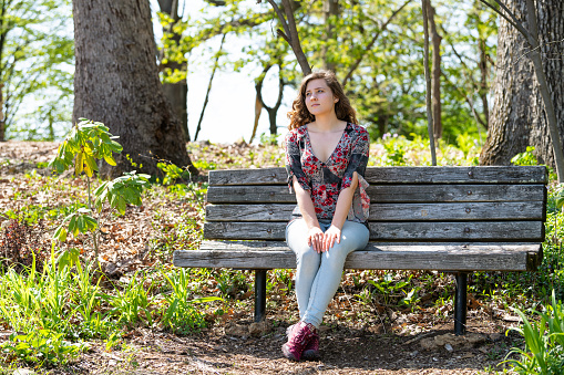 Woman in jeans sitting relaxing on a wooden bench in sunny forest during spring in Mill Mountain park in Roanoke, Virginia