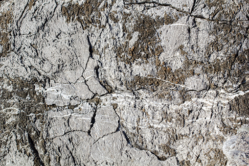 Natural stone background of gray marble veined granite with cracks and holes, porous and relief structure