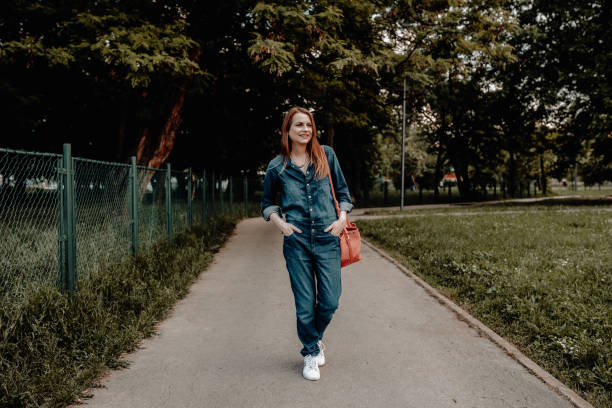Happy young woman enjoying a walk in the park Casual dressed woman wearing jumpsuit walking in the public park on a sunny summer day jumpsuit stock pictures, royalty-free photos & images