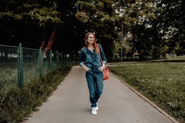Casual dressed woman wearing jumpsuit walking in the public park on a sunny summer day