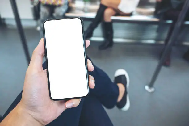 Photo of man's hand holding black mobile phone with blank screen in subway