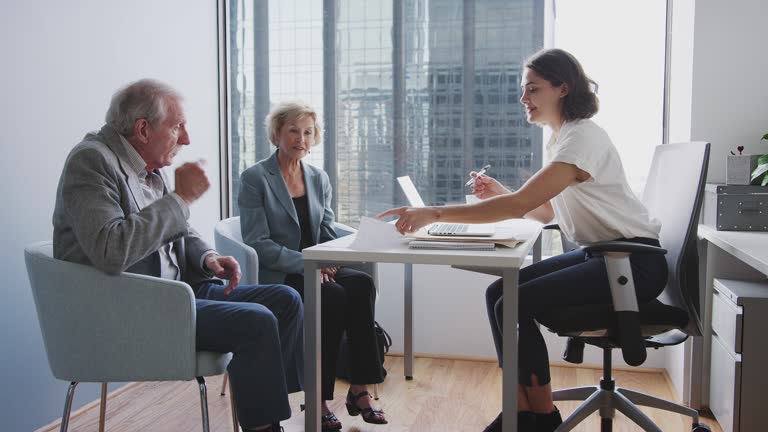 Senior Couple Signing Document In Meeting With Female Financial Advisor In Office