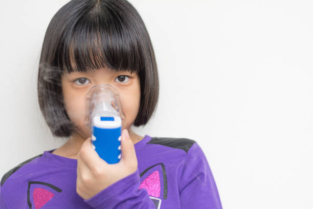 Beautiful sick girl inhalation therapy by the mask of inhaler . Close up image of a cute kid with respiratory problem or asthma with copy space. View of portable nebulizer with smoke from oxygen mask. hermosa terapia de inhalación de niña enferma por la mascarilla del inhalador. de cerca la imagen de un niño lindo con problemas respiratorios o asma con el espacio de copia. vista de nebulizador portátil con humo de la máscara de oxígeno.