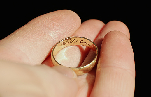 A man holds a wedding ring engraved 