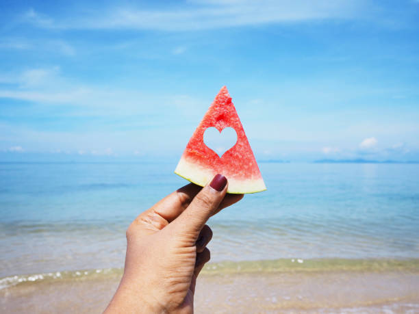 istock hand holding watermelon over summer beach background. 1153564092