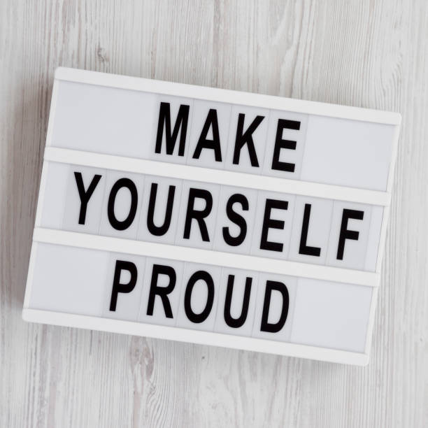 istock Light box with text 'Make yourself proud' on a white wooden background, top view. Flat lay, overhead, from above. 1153568219