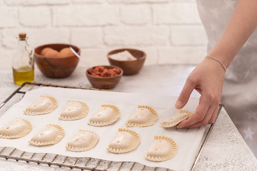 Woman put empanadillas , small filling tuna pies in roasting tray  to baked pastry in oven. Typical snack in  Latin American cultures  and Spain. Natural atmosphere lifestyle image.