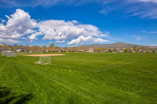 Soccer field and baseball field with view of mountain and cloudy blue sky. Houses and trees can also be seen around the perimeter of the sports field.