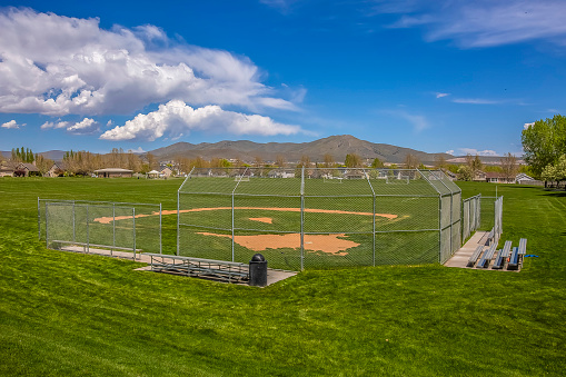 Softball or Baseball field with view of mountain and sky on a sunny day. Bleachers for players and spectators are installed behind the fence.