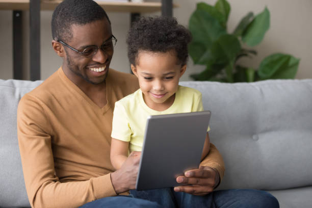 istock Black father teaching little son use tablet electronic device 1153592528