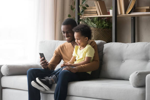 istock African father son sitting on couch having fun use smartphone 1153592530