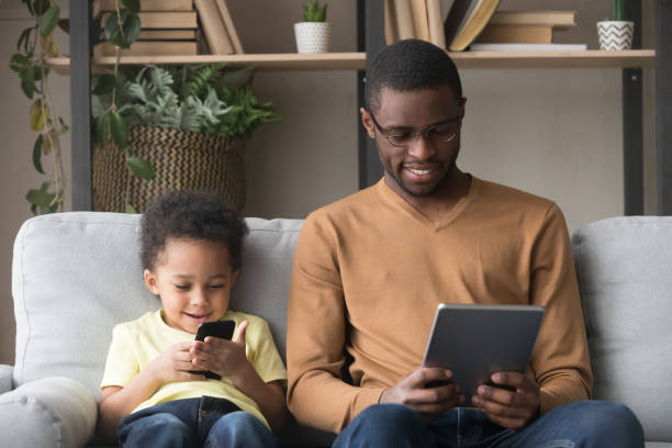 adicto a los gadgets padre africano y el hijo sentado en el sofá - african descent addiction african ethnicity rudeness fotografías e imágenes de stock