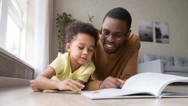 istock African father and son lying on warm floor reading book 1153592558
