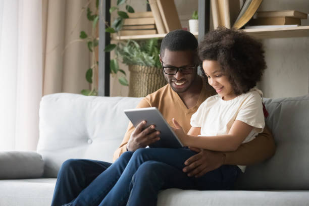 istock African father holds on lap daughter having fun use tablet 1153592566