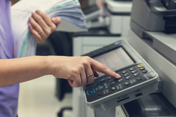 Bussinesswoman using copier machine to copy heap of paperwork in office.