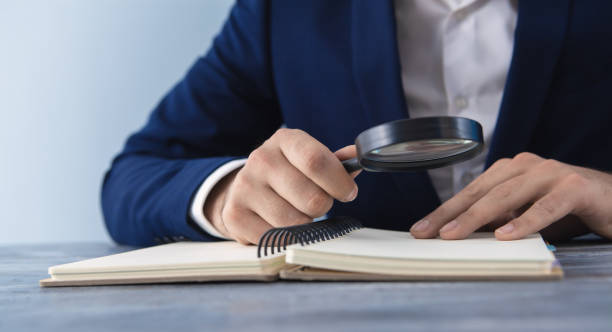 istock businessman holding a magnifying glass studying a book; looking for information; analysis; 1153593568