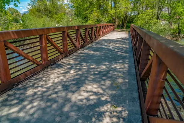 Bridge with brown guardrails overlooking a river and abundant trees. Scenic trail at Ogden River Parkway in Utah on a beautiful sunny day.