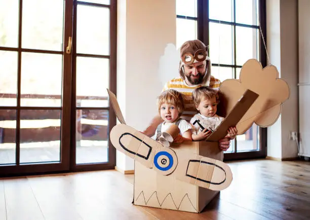 Photo of A father and toddler chidlren playing with carton plane indoors at home.