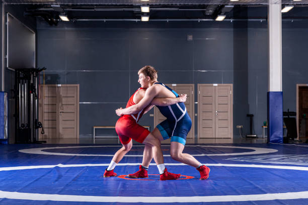 wrestlers Two strong wrestlers in blue and red wrestling tights are wrestlng and making a making a hip throw on a yellow wrestling carpet in the gym. Young man doing grapple. wrestling sport stock pictures, royalty-free photos & images