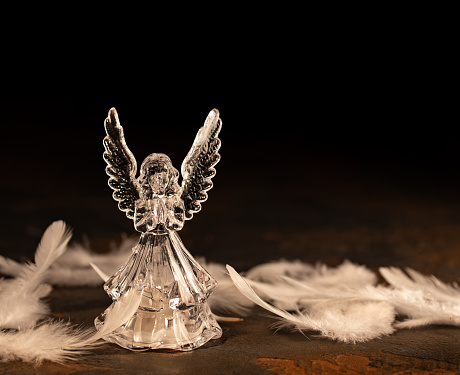 Glass angel with fallen feathers on a dark background