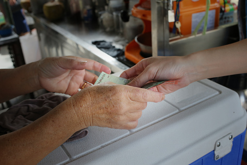 A senior lady accepting Malaysia currency notes at market stall.