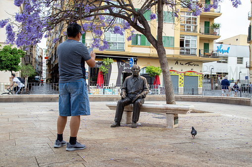 Malaga, Spain - May 24, 2019: A tourist taking a photo of the statue of painter and sculptor Pablo Picasso. It was made by Francisco Lopez Hernandez and was inaugurated in 2008.