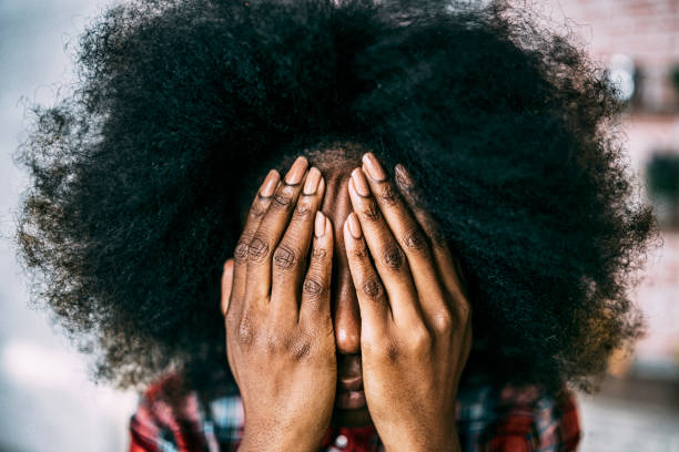African woman hiding her face with hands.