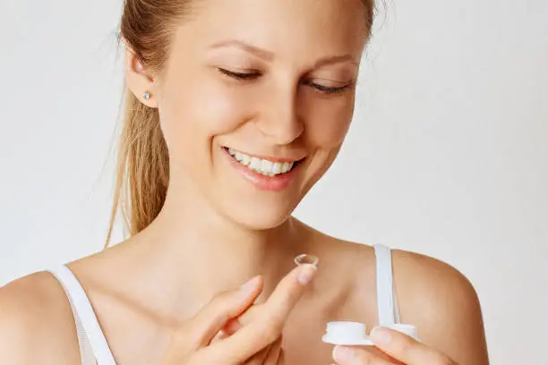 Photo of Young happy woman holds contact lens on her finger