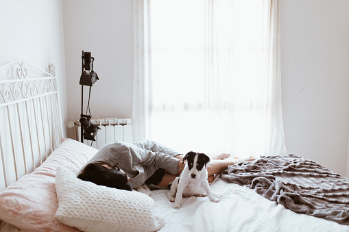 Sad brunette woman caressing her labrador puppy lying in bedroom