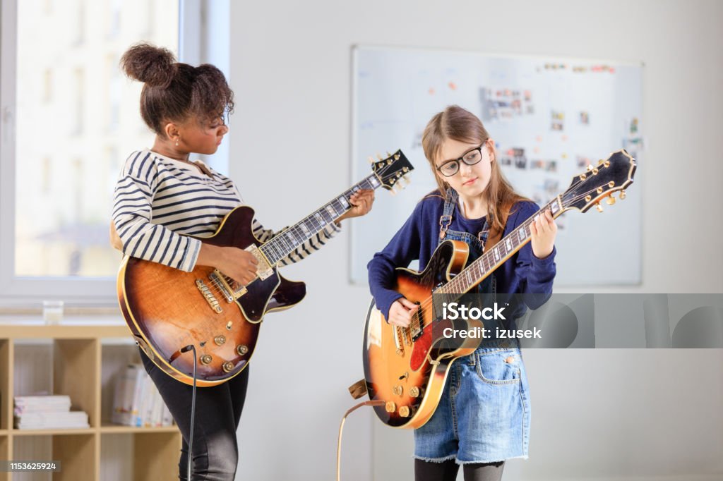 Female student learning guitar from trainer Girl playing electric guitar. Student is learning music from female guitarist. They are in training class at conservatory. Guitar Stock Photo