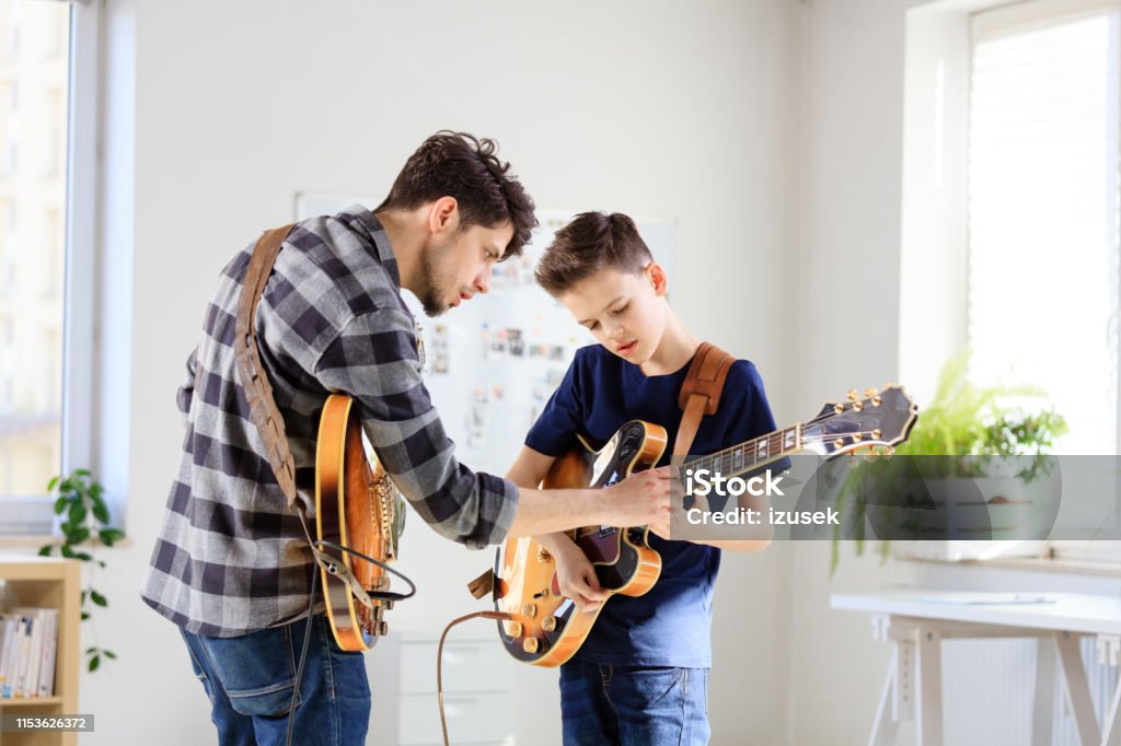 Teenage boy learning electric guitar from trainer Boy playing electric guitar. Student is learning music from male guitarist. They are in training class at conservatory. Education Training Class Stock Photo