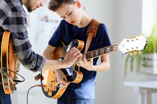 Boy playing electric guitar. Student is learning music from male guitarist. They are in training class at conservatory.