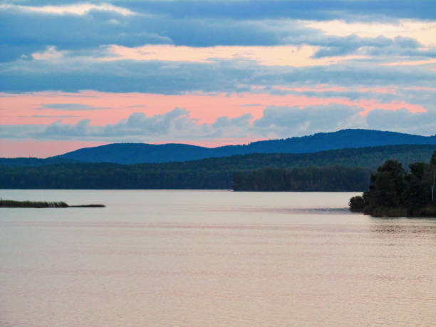 Beautiful reflection by a tranquil water of amazing sky and the lakeside at sundown in the summer evening. Lake Sungul, South Ural, Russia.