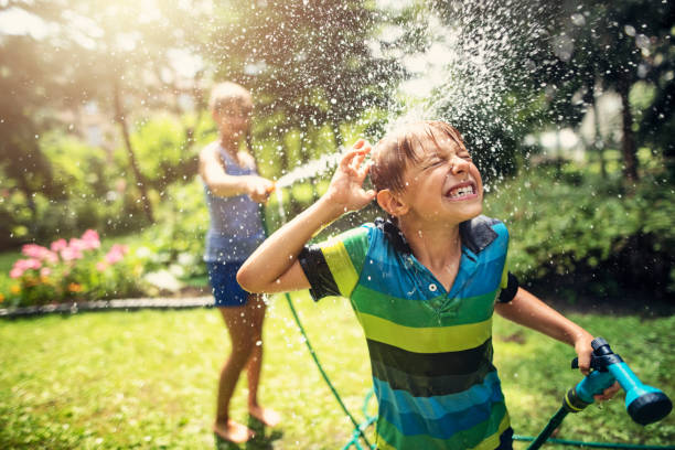 crianças que têm o divertimento da mangueira de jardim no pátio traseiro - mangueira de jardim - fotografias e filmes do acervo