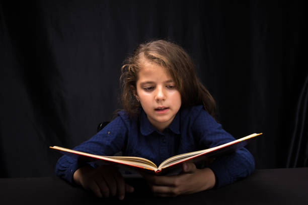 istock girl 8 years old reading a book on a dark background 1153639571