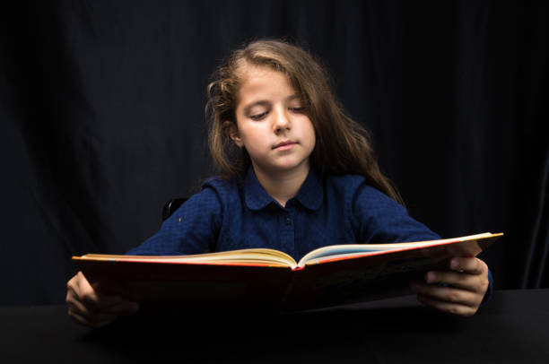 istock girl 8 years old reading a book on a dark background 1153639678