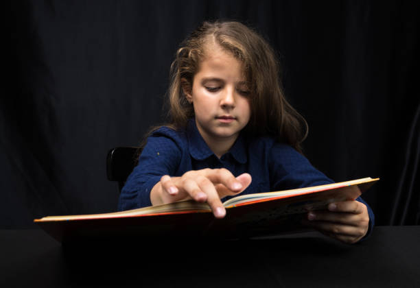 istock girl 8 years old reading a book on a dark background 1153639861