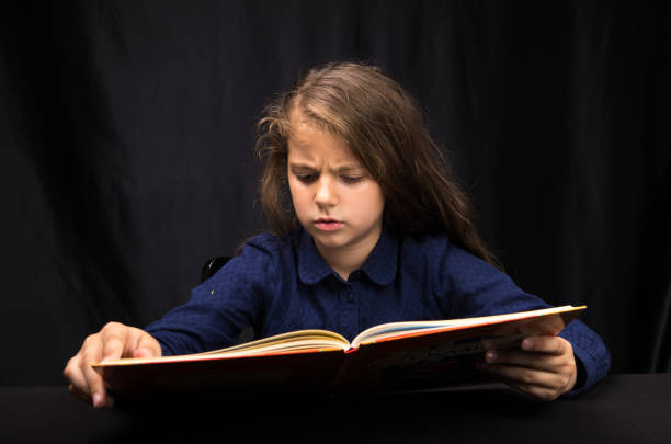istock girl 8 years old reading a book on a dark background 1153640063
