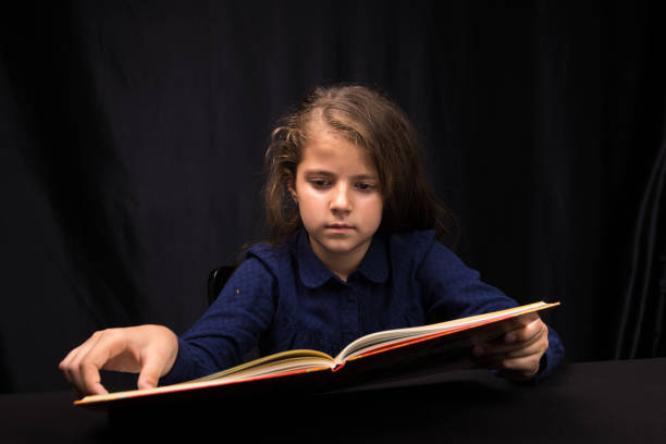 istock girl 8 years old reading a book on a dark background 1153640086