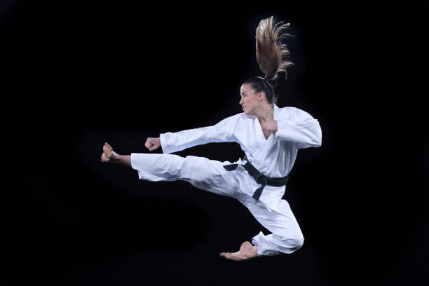 mujer en kimono realizando una patada voladora contra un fondo negro - kicking tae kwon do martial arts flying fotografías e imágenes de stock