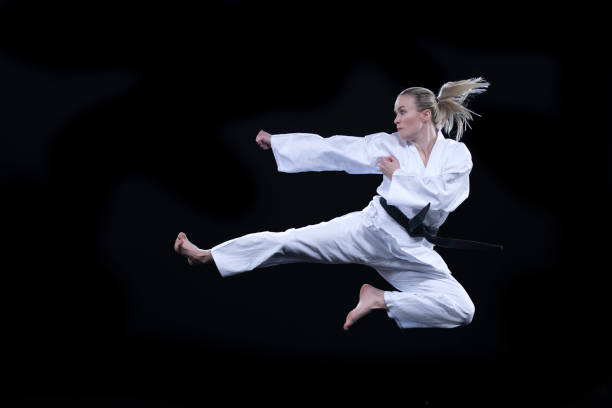 mujer en kimono realizando una patada voladora contra un fondo negro - kicking tae kwon do martial arts flying fotografías e imágenes de stock