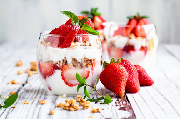 Healthy breakfast of strawberry parfaits made with fresh fruit, yogurt and granola Healthy breakfast of strawberry parfaits made with fresh fruit, yogurt and granola over a rustic white table. Shallow depth of field with selective focus on glass jar in front. Blurred background. parfait photos stock pictures, royalty-free photos & images
