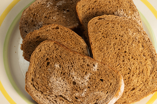 Sliced rye bread covered with mold is placed on the table with a white background. Bread lies on a plate. Photo view from above.