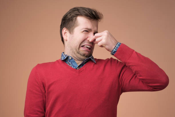 man plugs nose as smells something stink - facial expression unpleasant smell shirt caucasian imagens e fotografias de stock