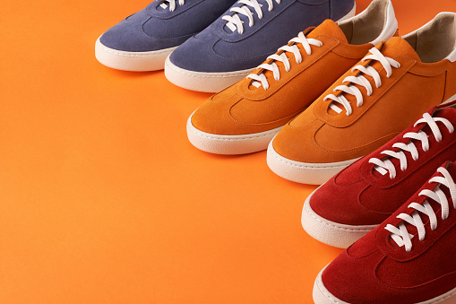 Colorful casual unisex suede sneakers standing in line on orange background with copy space, deep depth of field